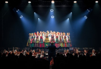 Na scenie Artyści w kostiumach opoczyńskich w trakcie wykonywania choreografii tanecznej, widoczna orkiestra w kostiumach wilanowskich