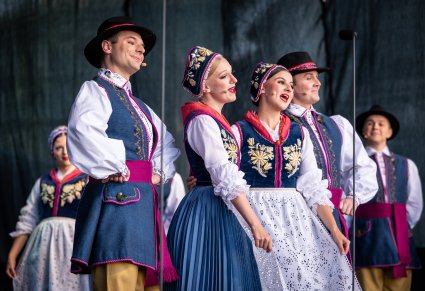 Na pierwszym planie czwórka Artystów w trakcie śpiewania na scenie w kostiumach kaszubskich