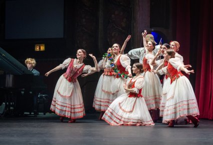 Grupa Artystem Baletu w kostiumach stylizowanych w trakcie wykonywania choreografii tanencznej. Widoczny Muzyk grający na fortepianie