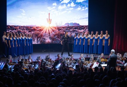 Na środku sceny Solista Chóru w trakcie śpiewu, Po bokach sceny Artyści Chóru we współczesnych kostiumach, niżej sceny Artyści Orkiestry  w kostiumach wilanowskich