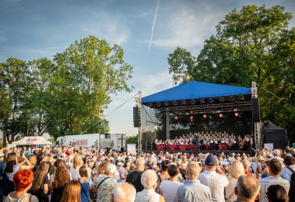 Widok na scenę na której są Artyści, widać również publiczność a po lewej stronie sceny stoją samochody techniczne MAZOWSZE