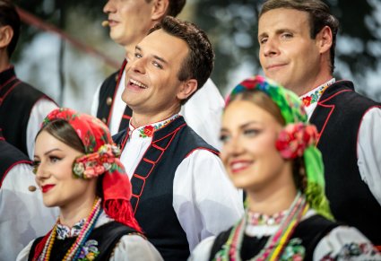 Zbliżenie na uśmiechniętych Artystów z chóru w kostiumach łowickich