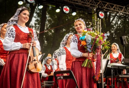 Uśmiechnięte Muzyczki z orkiestry na scenie po zakończonym koncercie. Jedna z nich trzyma kwiaty