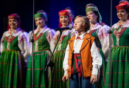 Zbliżenie na śpiewającego uczestnika gali a w tle chór zespołu "Mazowsze" w kostiumach kurpiowskich