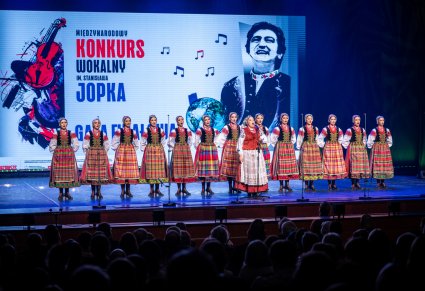 Śpiewająca uczestniczka gali a w tle chór zespołu "Mazowsze" w kostiumach podlaskich na scenie