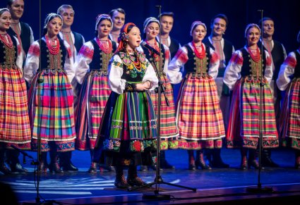 Śpiewająca uczestniczka gali a w tle chór zespołu "Mazowsze" w kostiumach podlaskich na scenie