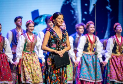 Konferansjer Katarzyna Sanocka a w tle artyści zespołu "Mazowsze" na scenie