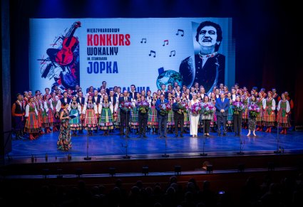 Skład jury z kwiatami na scenie a za nim zespół "Mazowsze"