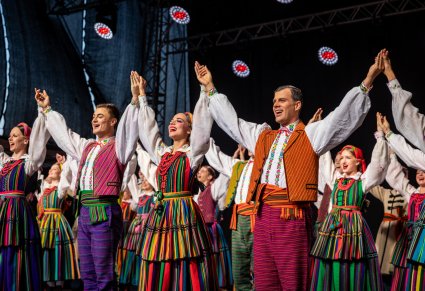 Artyści trzymający się za ręce w górze z szerokimi uśmiechami w kostiumach opoczyńskich