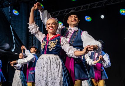 Uśmiechnięci Artyści w kostiumach kaszubskich na scenie wykonujący choreografię taneczną