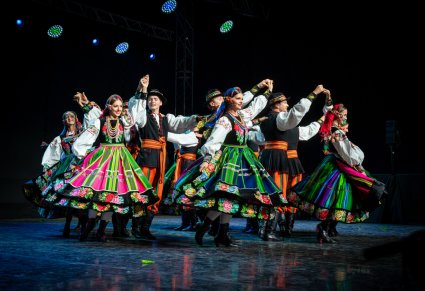Artyści na scenie w kostiumach łowickich wykonujący choreografię taneczną