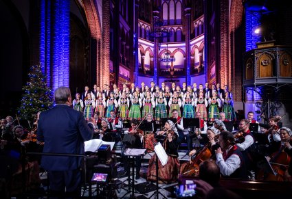 chór i orkiestra w trakcie koncertu kolędowego a przed nimi dyrygen