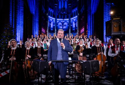 Maestro Jacek Boniecki przemawia na tle orkiestry i chóru do publiczności