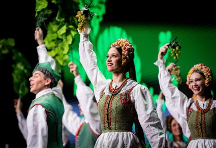 Zbliżenie na artystkę w kostiumie lubuskim trzymającą w uniesionej ręce kiść winogron