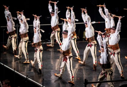 Artyści zespołu Mazowsze w kostiumach góralskich tańczą na scenie z ciupagami uniesionymi w górze