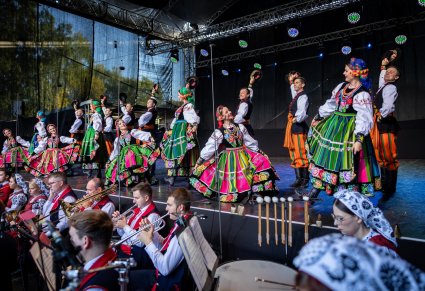 Artyści w kostiumach łowickich w finałowym układzie, przed sceną widoczna orkiestra