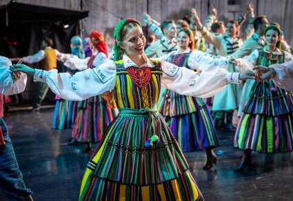 Zbliżenie na tancerkę w kostiumie opoczyńskim na scenie, w tle reszta zespołu
