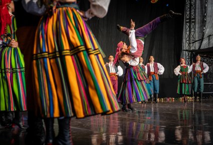 Zbliżenie na spódnicę kostiumu opoczyńskiego, w tle tancerz w akrobacji tanecznej