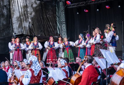 Artyści w kostiumach limanowskich na scenie, przed nimi widoczna orkiestra