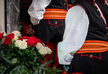 Zbliżenie na biało czerwone róże i kostiumy łowickie mężczyzn