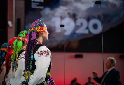 Zbliżenie Na Artystki z chóru w kostiumach łowickich w tle napis 1920 i Dyrektor Jacek Boniecki