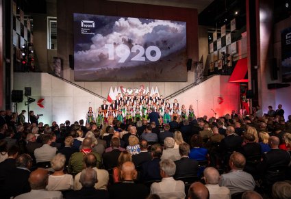 Na pierwszym planie publiczność w tle Chór w kostiumach łowickich  w czterech rzędach a na ścianie napis 1920