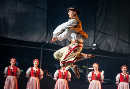Zbliżenie na tancerza w kostiumie jurgowskim podczas tańca na scenie, w tle widoczne tancerki w kostiumach jurgowskich
