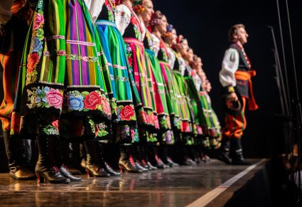 Zbliżenie na spódnice i buty kostiumu łowickiego, w tle widoczny solista chóru