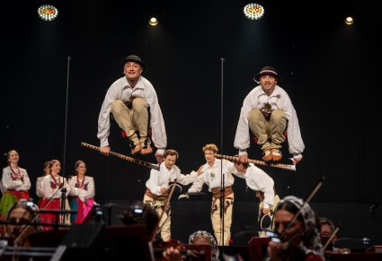 Dwóch artystów baletu w kostiumach podhalańskich skacze przez ciupagi