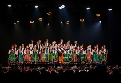 Chór w kostiumach łowickich śpiewa na scenie a z centralnym punkcie solista śpiewający Furmana