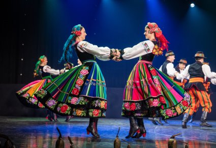 Dwie artystki w kostiumach łowickich kręcą się ze sobą trzymając za ręce