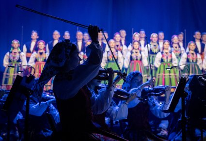 Zbliżenie na skrzypaczkę podczas koncertu, w tle widoczna orkiestra i chór