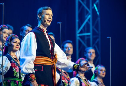 Zbliżenie na solistę chóru podczas koncertu z widocznych chórem w tle