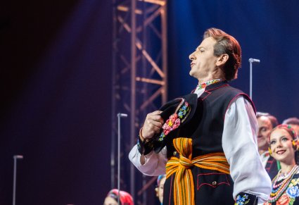 Zbliżenie na solistę chóru podczas koncertu z widocznych chórem w tle