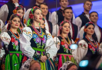 Zbliżenie na śpiewającą solistkę a za nią chór w kostiumach łowickich