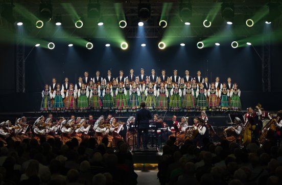  Na scenie Artyści Chóru w kostiumach łowickich, niżej Orkiestra w kostiumach wilanowskich wraz z Dyrygentem, oraz widoczna część Publiczności