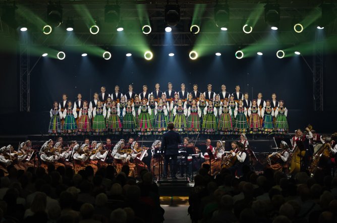  Na scenie Artyści Chóru w kostiumach łowickich, niżej Orkiestra w kostiumach wilanowskich wraz z Dyrygentem, oraz widoczna część Publiczności