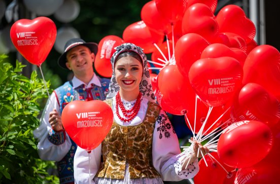  Para Artystów na VIII Rodzinnym Pikniku w strojach ludowych trzymająca w ręku czerwone balony w kształcie serca