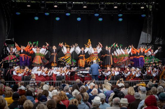  Artyści na scenie w kostiumach ludowych z widoczną orkiestrą i publicznością