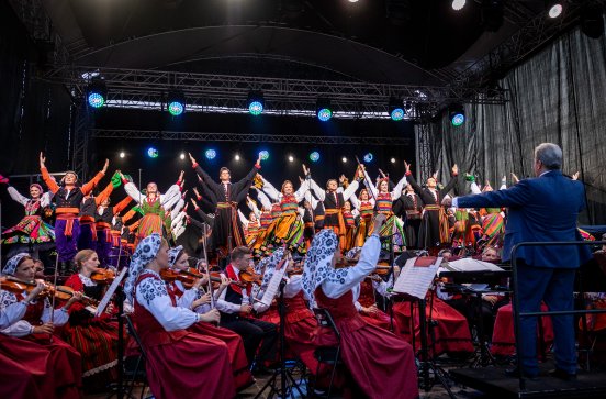  Artyści w kostiumach ludowych na scenie z widoczną orkiestrą