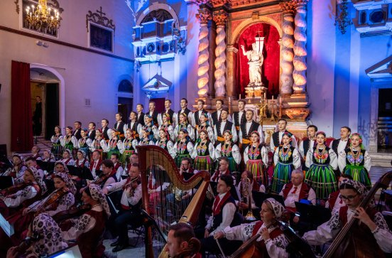  Na pierwszym planie chór ubrany w kostiumy łowickie, za nim ołtarz kościelny. Przed chórem Orkiestra z instrumentami