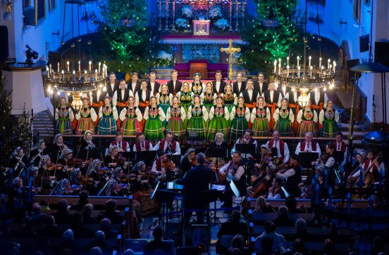  Na pierwszym planie Artyści Chóru w kostiumach łowickich przed nimi orkiestra wraz z Dyrektorem Jackiem Bonieckim, który dyryguje koncert. Widoczna jest również przyciemniona publiczność
