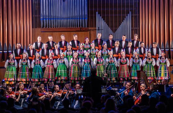  Na scenie Artyści chóru w kostiumach łowickich ustawionych w rzędach, pod sceną Orkiestra w kostiumach wilanowskich pod dyrekcją maestro Jacka Bonieckiego