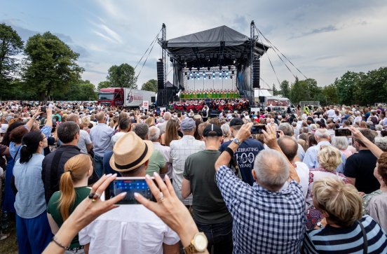  Publiczność skierowana w stronę sceny. Na scenie Artyści chóru w kostiumach kostiumach kurpiowskich wraz z orkiestrą w kostiumach wilanowskich