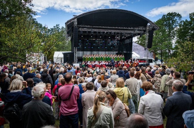  Scena plenerowa w Choszczówce ze zgromadzoną Publicznością, na scenie Orkiestra w kostiumach Wilanowskich wraz z Dyrygentem i Artyści Chóru w kostiumach kurpiowskich