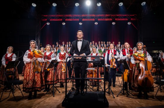  Na pierwszym planie dyrygent, za nim orkiestra a w tle widoczny chór w kostiumach łowickich