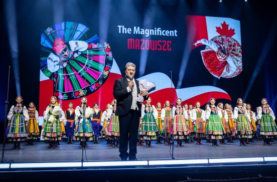  Na pierwszym planie Dyrektor zespołu trzymający bukiet kwiatów, w tle Artyści w kostiumach z finałowego numeru koncertu